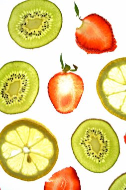 Portakal, çilek ve kivi gibi farklı dilimlenmiş meyveler parlak beyaz bir arka plan üzerinde yatıyor ve ışık ile yukarıdan aydınlatılır - farklı renklerde taze ve sağlıklı meyve kavramı - 