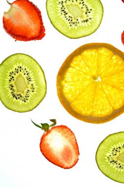 Portakal, çilek ve kivi gibi farklı dilimlenmiş meyveler parlak beyaz bir arka plan üzerinde yatıyor ve ışık ile yukarıdan aydınlatılır - farklı renklerde taze ve sağlıklı meyve kavramı