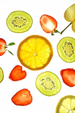 Portakal, çilek ve kivi gibi farklı dilimlenmiş meyveler parlak beyaz bir arka plan üzerinde yatıyor ve ışık ile yukarıdan aydınlatılır - farklı renklerde taze ve sağlıklı meyve kavramı