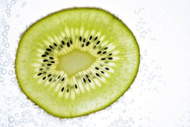 Bir dilimlenmiş kivi hafif bir arka plan üzerinde yatıyor - ince kivi dilimleri ile aşağıdan aydınlatılır 