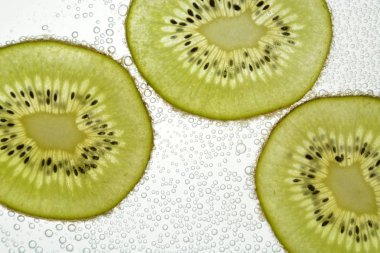 Bir dilimlenmiş kivi hafif bir arka plan üzerinde yatıyor - ince kivi dilimleri ile aşağıdan aydınlatılır 