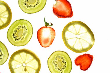 Portakal, çilek ve kivi gibi farklı dilimlenmiş meyveler parlak beyaz bir arka plan üzerinde yatıyor ve ışık ile yukarıdan aydınlatılır - farklı renklerde taze ve sağlıklı meyve kavramı - 