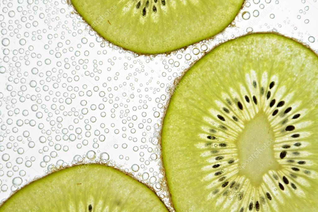 A sliced kiwi lies on a light background - through the thin kiwi slices are illuminated from below 