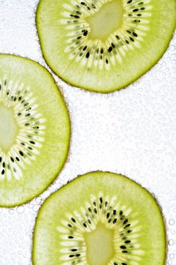 Bir dilimlenmiş kivi hafif bir arka plan üzerinde yatıyor - ince kivi dilimleri ile aşağıdan aydınlatılır 