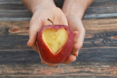 Elinde kesilmiş bir kalp şekli ile elma tutma