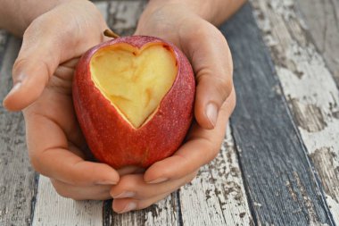 Elinde kesilmiş bir kalp şekli ile elma tutma