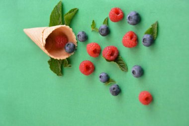 Ferahlatıcı bir yaz meyveli dondurma sembolü olarak renkli bir arka plan üzerinde yaban mersini, ahududu ve nane ile bir dondurma konisi