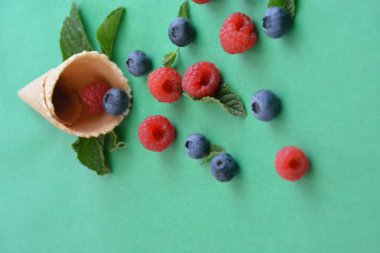 Ferahlatıcı bir yaz meyveli dondurma sembolü olarak renkli bir arka plan üzerinde yaban mersini, ahududu ve nane ile bir dondurma konisi