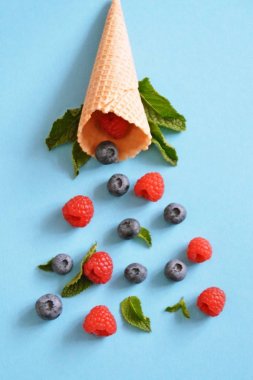 Ferahlatıcı bir yaz meyveli dondurma sembolü olarak renkli bir arka plan üzerinde yaban mersini, ahududu ve nane ile bir dondurma konisi