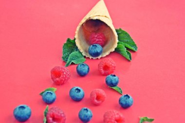 Ferahlatıcı bir yaz meyveli dondurma sembolü olarak renkli bir arka plan üzerinde yaban mersini, ahududu ve nane ile bir dondurma konisi