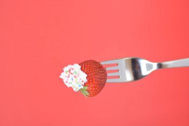 Renkli bir arka plan önünde krem ile bir çatal ucunda Çilek 