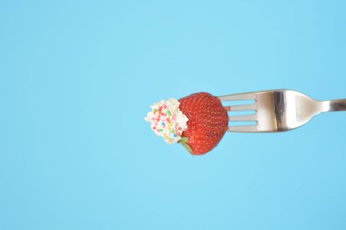 Renkli bir arka plan önünde krem ile bir çatal ucunda Çilek 