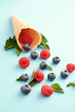 Ferahlatıcı bir yaz meyveli dondurma sembolü olarak renkli bir arka plan üzerinde yaban mersini, ahududu ve nane ile bir dondurma konisi