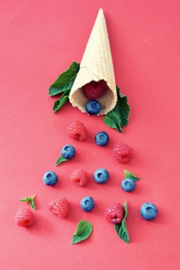 Ferahlatıcı bir yaz meyveli dondurma sembolü olarak renkli bir arka plan üzerinde yaban mersini, ahududu ve nane ile bir dondurma konisi