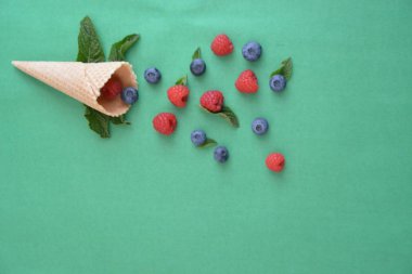 Ferahlatıcı bir yaz meyveli dondurma sembolü olarak renkli bir arka plan üzerinde yaban mersini, ahududu ve nane ile bir dondurma konisi