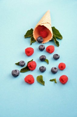 Ferahlatıcı bir yaz meyveli dondurma sembolü olarak renkli bir arka plan üzerinde yaban mersini, ahududu ve nane ile bir dondurma konisi