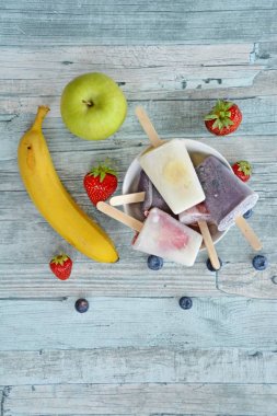 Bir ferahlık olarak yaz için mükemmel bir ahşap arka planda çilek, yaban mersini, elma ve muz ile ev yapımı dondurma