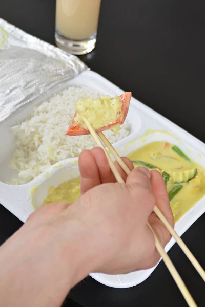 Close-up: eat yellow curry with rice from a styrofoam box with chopsticks