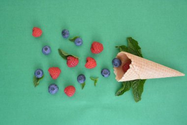 Ferahlatıcı bir yaz meyveli dondurma sembolü olarak renkli bir arka plan üzerinde yaban mersini, ahududu ve nane ile bir dondurma konisi