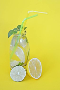 Düz bir arka plan karşı yaz aylarında meyveli bir ferahlık olarak su dolu bir şişe limon, nane ve limon parçaları