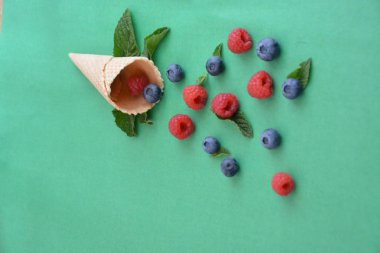 Ferahlatıcı bir yaz meyveli dondurma sembolü olarak renkli bir arka plan üzerinde yaban mersini, ahududu ve nane ile bir dondurma konisi