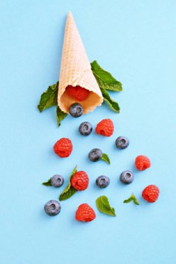 Ferahlatıcı bir yaz meyveli dondurma sembolü olarak renkli bir arka plan üzerinde yaban mersini, ahududu ve nane ile bir dondurma konisi