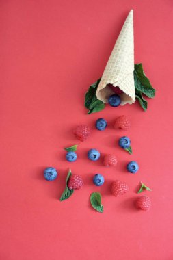 Ferahlatıcı bir yaz meyveli dondurma sembolü olarak renkli bir arka plan üzerinde yaban mersini, ahududu ve nane ile bir dondurma konisi