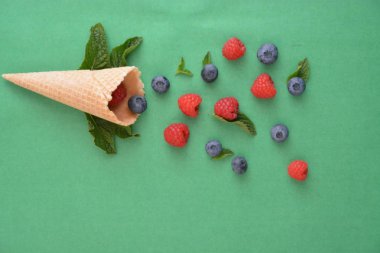 Ferahlatıcı bir yaz meyveli dondurma sembolü olarak renkli bir arka plan üzerinde yaban mersini, ahududu ve nane ile bir dondurma konisi