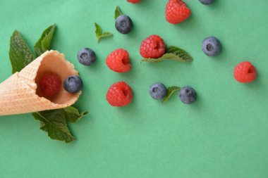 Ferahlatıcı bir yaz meyveli dondurma sembolü olarak renkli bir arka plan üzerinde yaban mersini, ahududu ve nane ile bir dondurma konisi