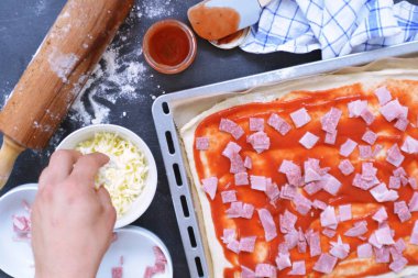 Yakın çekim-Man, jambon, salam ve peynir pişirme levha yanında malzemeler ile pizza hamur dolu bir pizza dolduruyor 