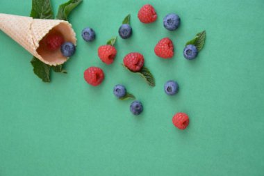 Ferahlatıcı bir yaz meyveli dondurma sembolü olarak renkli bir arka plan üzerinde yaban mersini, ahududu ve nane ile bir dondurma konisi