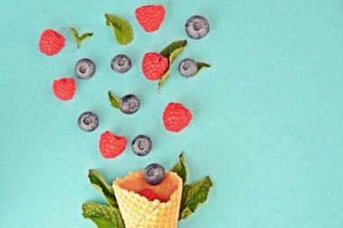 Ferahlatıcı bir yaz meyveli dondurma sembolü olarak renkli bir arka plan üzerinde yaban mersini, ahududu ve nane ile bir dondurma konisi