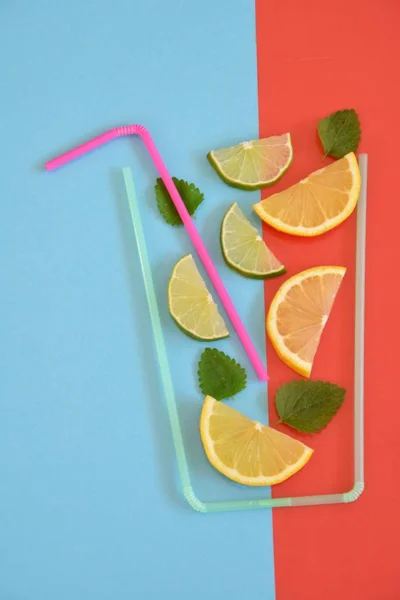 Creative layout strawberry lemonade ingredients - lemon, citrus, ice falling in glass made with cocktail straws on colorful background. Summer drinks. Minimal food concept. Selective focus.