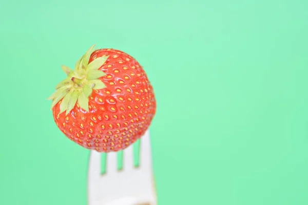 Strawberry on the tip of a fork in front of a colorful background