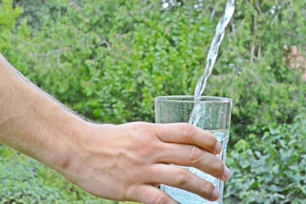 Свежая Чистая Вода Течет Стакане Перед Зеленым Летним Фоном Держится — стоковое фото