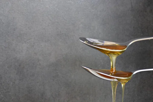 蜂蜜は黒を背景にスプーンの上を流れる — ストック写真