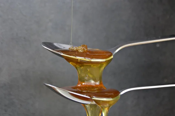 Honey flows over spoon on black background
