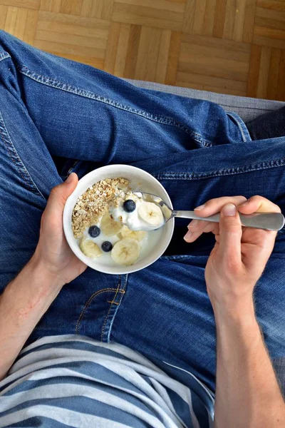 close up - man eat healthy breakfast with oatmeal, bananas, blueberries and yoghurt