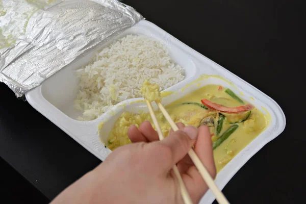 Close-up: eat yellow curry with rice from a styrofoam box with chopsticks