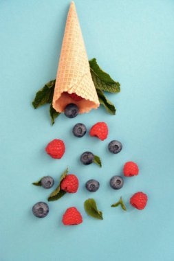 Ferahlatıcı bir yaz meyveli dondurma sembolü olarak renkli bir arka plan üzerinde yaban mersini, ahududu ve nane ile bir dondurma konisi