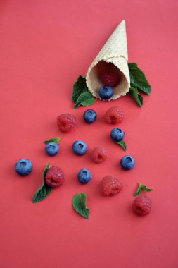 Ferahlatıcı bir yaz meyveli dondurma sembolü olarak renkli bir arka plan üzerinde yaban mersini, ahududu ve nane ile bir dondurma konisi