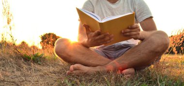 Yakın çekim - güneş bir ormanın yakınında arka planda batarken ayakkabı ve şort olmadan kırsal bir kitap okuma adam - okuma sevgisi için kavram 
