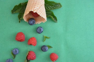 Ferahlatıcı bir yaz meyveli dondurma sembolü olarak renkli bir arka plan üzerinde yaban mersini, ahududu ve nane ile bir dondurma konisi