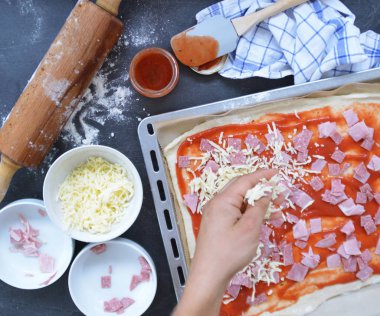 Yakın çekim-Man, jambon, salam ve peynir pişirme levha yanında malzemeler ile pizza hamur dolu bir pizza dolduruyor 