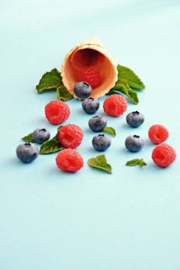 Ferahlatıcı bir yaz meyveli dondurma sembolü olarak renkli bir arka plan üzerinde yaban mersini, ahududu ve nane ile bir dondurma konisi