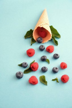 Ferahlatıcı bir yaz meyveli dondurma sembolü olarak renkli bir arka plan üzerinde yaban mersini, ahududu ve nane ile bir dondurma konisi