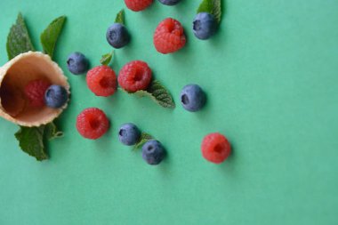 Ferahlatıcı bir yaz meyveli dondurma sembolü olarak renkli bir arka plan üzerinde yaban mersini, ahududu ve nane ile bir dondurma konisi