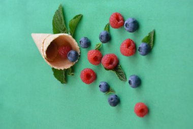 Ferahlatıcı bir yaz meyveli dondurma sembolü olarak renkli bir arka plan üzerinde yaban mersini, ahududu ve nane ile bir dondurma konisi