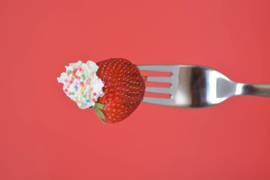 Renkli bir arka plan önünde krem ile bir çatal ucunda Çilek