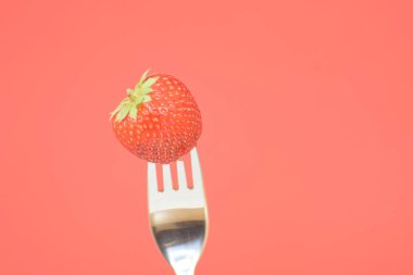 Renkli bir arka plan önünde bir çatal ucunda Çilek